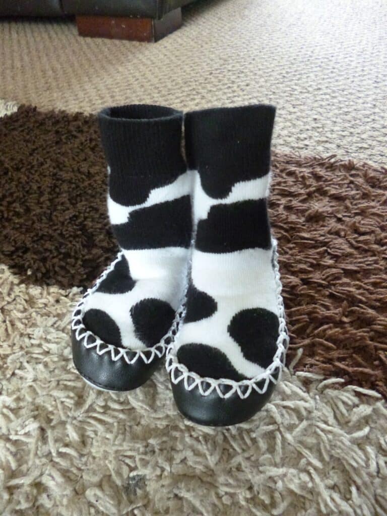 A pair of slipper socks with black soles and black-and-white cow print pattern stand upright on a textured rug.