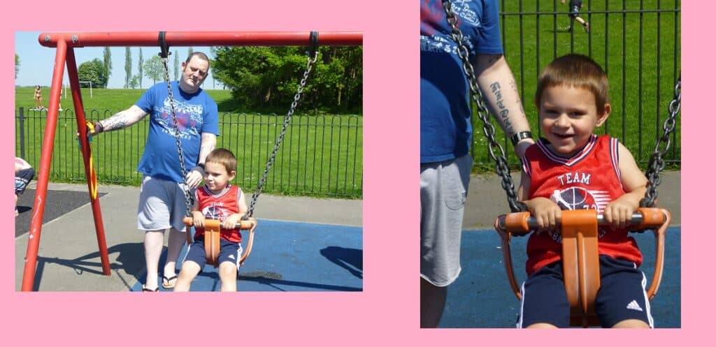 A man pushes a young boy on a swing at a park playground. The boy, wearing a red basketball vest, smiles while swinging. The background shows a fence, grass, and trees under a sunny sky—perfect for Family Activities.