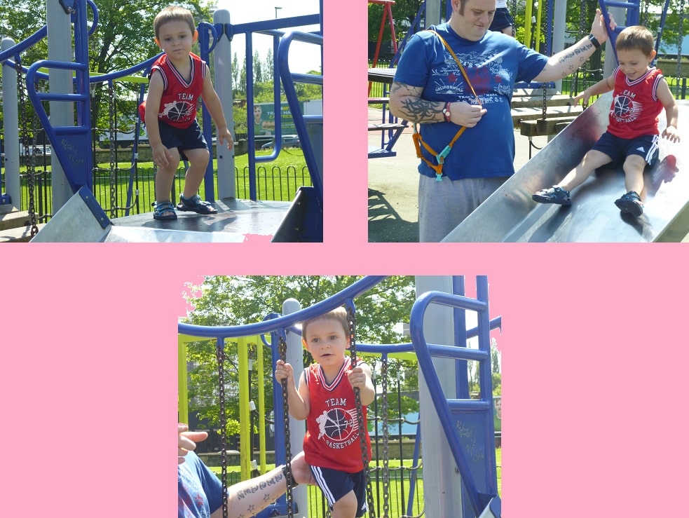 A young boy in a red basketball vest enjoys the slide and climbing equipment at a park playground with an adult, surrounded by trees and playground structures—a perfect spot for Family Day and fun family activities under the sunny sky.