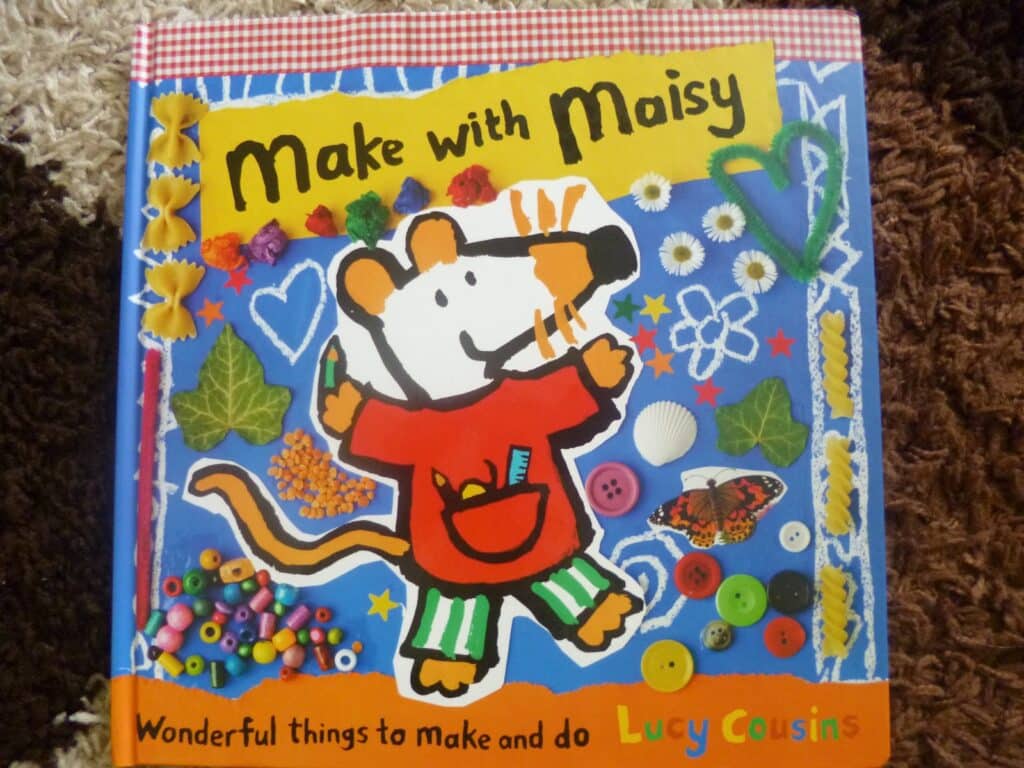 The image shows the cover of the Maisy craft book "Make with Maisy" by Lucy Cousins, featuring an illustrated mouse named Maisy surrounded by craft items like buttons, beads, shells, and flowers on a colourful background.