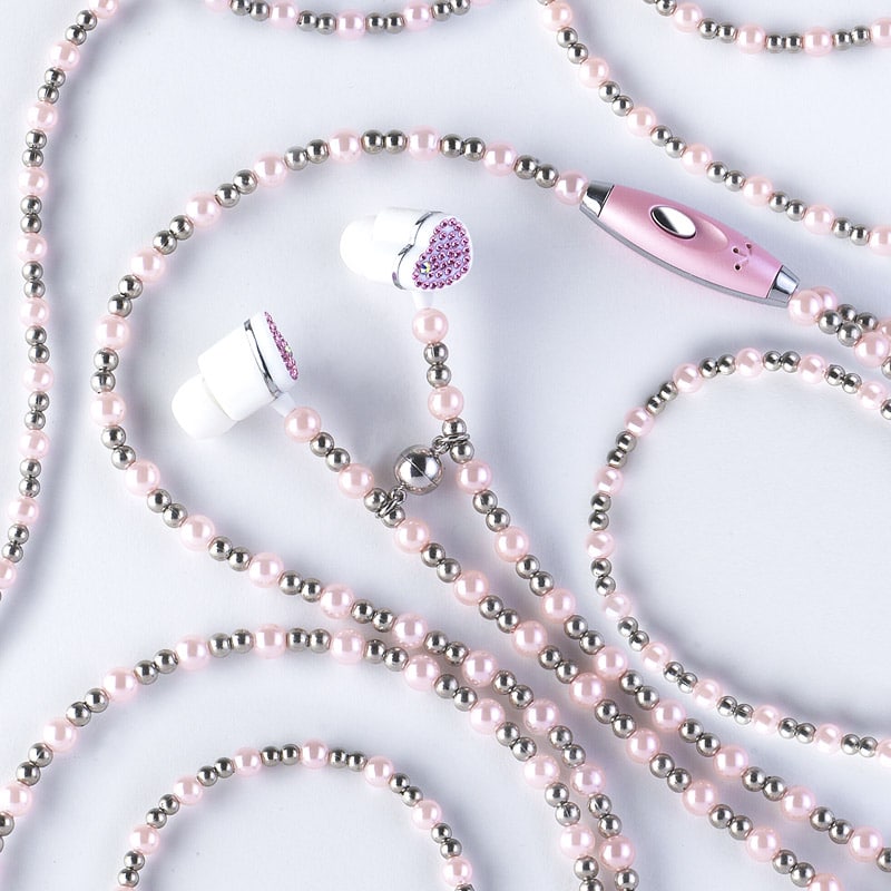 Pink and silver beaded Jewelfone earphones and a matching pink device are laid out on a white surface, their cords forming loops and curves among scattered beads, capturing a sense of playful passion.
