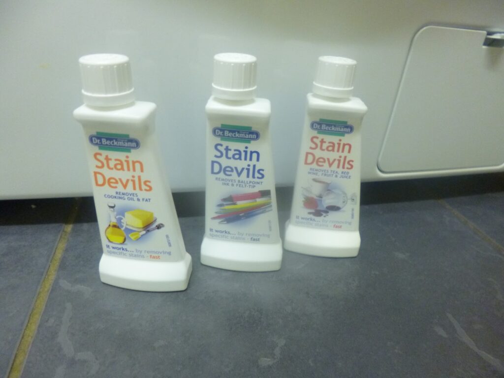 Three bottles of Dr Beckmann Stain Devils, top-quality cleaning products, are lined up on a tiled floor with colourful labels, each stain remover designed for tackling specific types of stains.