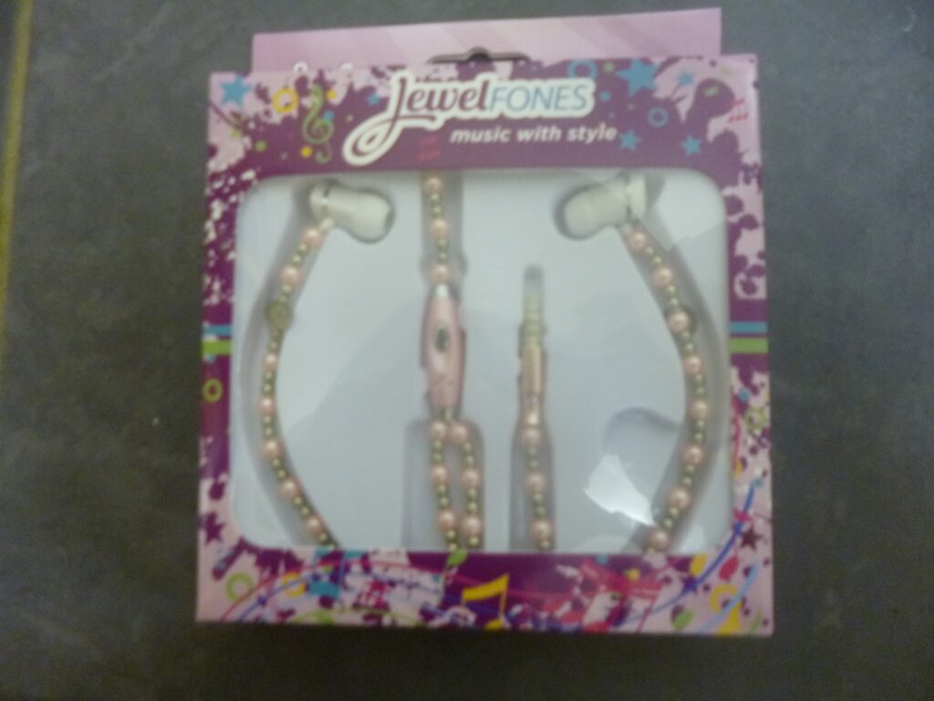 A box of Jewelfone earphones, decorated with pink beads and packaged in a purple and pink box with musical notes and colourful designs. The text on the box says "Jewel Fones—music with passion and style.