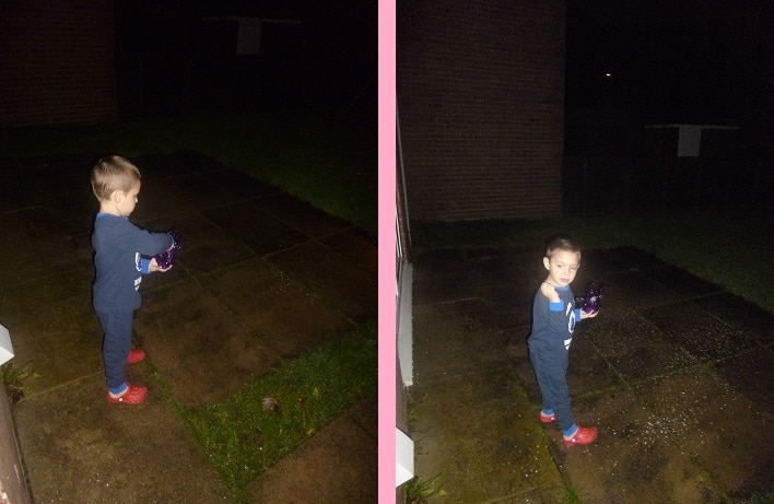 On Christmas Day in 2012, a young child in pyjamas and red slippers stands outside at night on a wet patio, holding a purple object, with a grassy area and building visible in the background.