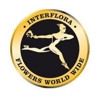 A gold and black circular Interflora logo featuring a running figure holding flowers, with the words "INTERFLORA FLOWERS WORLD WIDE" around the edge—perfect for sending love this Valentines Day.