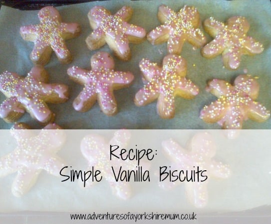 Ten gingerbread-shaped vanilla biscuits with pink icing and colourful sprinkles are arranged on a baking tray. The text overlay reads, "Recipe: Simple Vanilla Biscuits," with a biscuit recipe website link at the bottom.