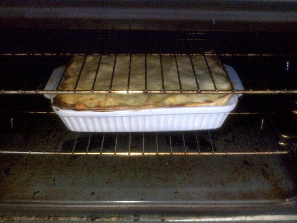 A rectangular casserole dish with golden-brown baked lasagne sits on an oven shelf inside the oven.
