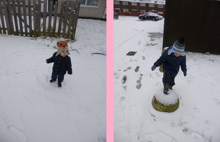 Two young children bundled in winter clothes and hats play outside in the snow. On the left, a child stands in the snow; on the right, another stands atop a snow-covered concrete post. The scene captures a joyful Let It Snow moment.
