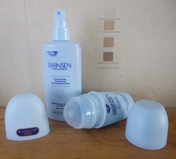 Two Bionsen deodorants are displayed on a wooden surface: a Pump Spray stands upright, while a Roll On lies down with its cap off. Both are labelled “aluminium free,” with their caps placed neatly beside each deodorant.