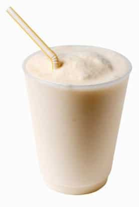 A vanilla and banana milkshake in a clear plastic cup with a yellow-striped straw, perfect for breakfast, isolated on a white background.
