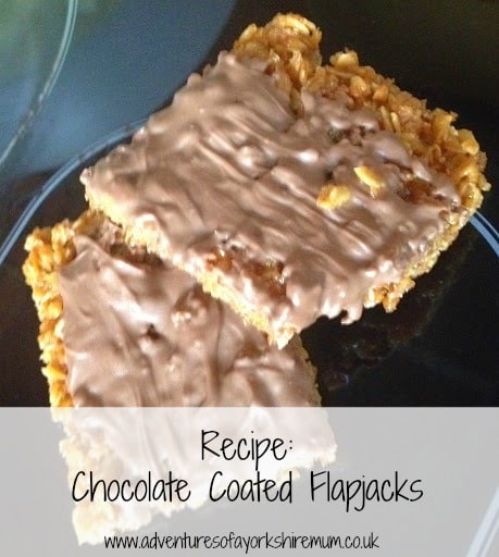 Two homemade chocolate-coated flapjacks sit on a plate, showcasing their rich, melted topping. Text below: "Recipe: Chocolate Flapjacks www.adventuresofyorkshiremum.co.uk".