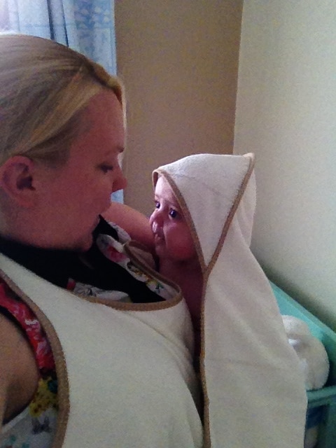 A woman holding a baby wrapped in a Cuddledry Baby Towel with a Gingham Edge. They face each other, sharing an affectionate moment in a softly lit room.
