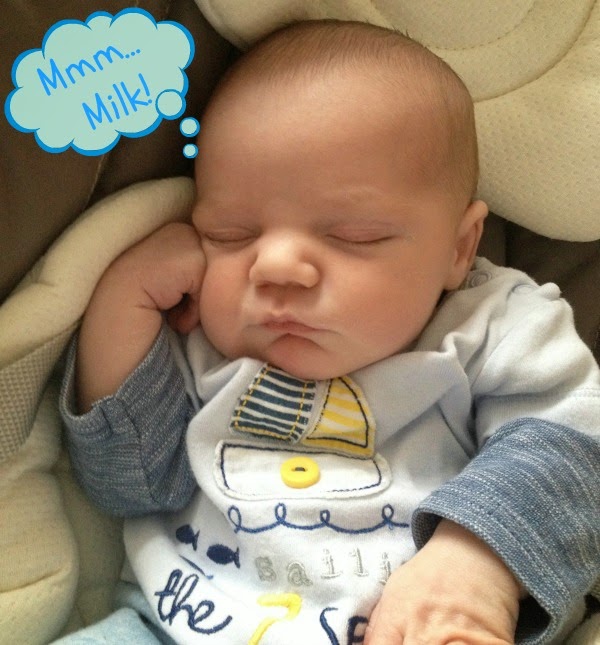 A baby is sleeping peacefully with one hand resting on their cheek, wearing a light blue outfit with a sailboat design. Itβs as if dreaming of a baby story, while a thought bubble reads, "Mmm... Milk!.