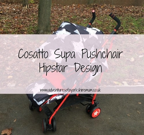 A black and white star-patterned Cosatto Supa Hipstar pushchair with red handles and wheels is parked outdoors on a path next to trees. Text overlay reads: "Cosatto Supa Pushchair Hipstar Design.