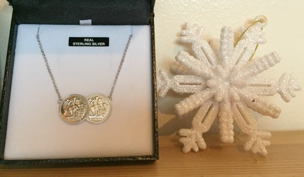 A sterling silver necklace with two round pendants displayed in a jewellery box sits next to a glittery white snowflake ornament—an elegant choice for Christmas presents on a wooden surface.