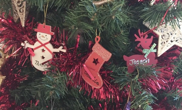 Three Christmas tree baubles—a snowman labelled "Thomas," a stocking labelled "Charlie," and a reindeer labelled "Joseph"—hang among festive Christmas decorations, reflecting a true love of Christmas on the beautifully adorned tree.