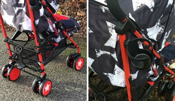 Close-up view of a Cosatto pushchair with a red and black frame, red wheels featuring white stars, and a black and white patterned canopy. The Cosatto Supa pushchair is on a paved outdoor surface.
