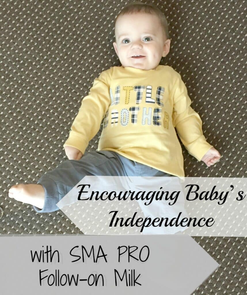 A smiling baby in a yellow shirt and blue trousers lies on a brown dotted carpet. Overlaid text reads: "Nurture baby's independence with SMA PRO Follow-on Milk.