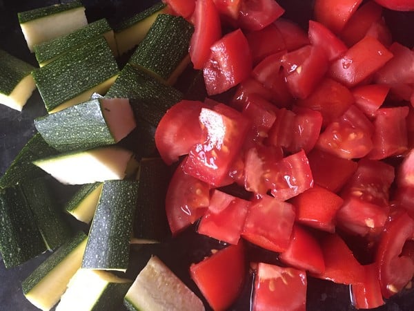 Chopped courgette and diced tomatoes from HelloFresh are placed side by side on a dark surface, ready for cooking or mixing.