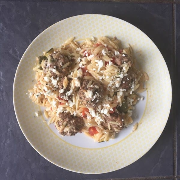 A plate of orzo pasta mixed with meatballs, diced vegetables, and topped with crumbled white cheese, served on a patterned white and yellow plate—just like a delicious HelloFresh creation.