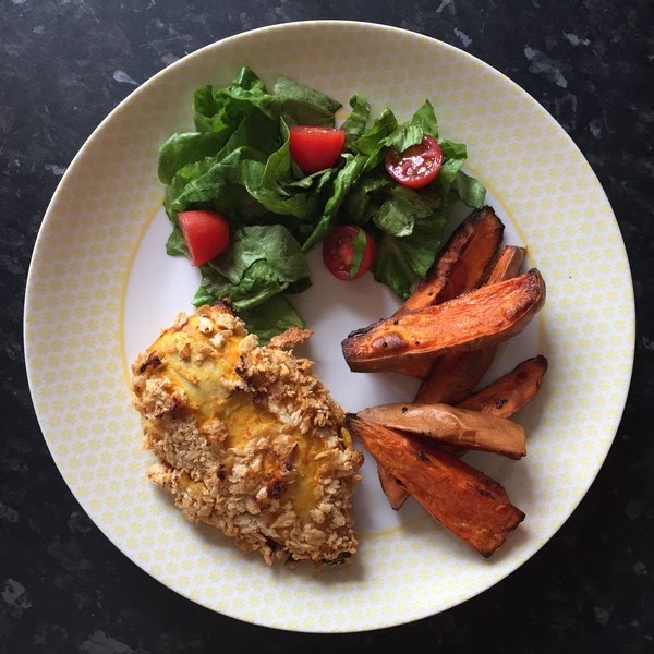 A plate with breaded baked chicken, sweet potato wedges, and a fresh salad of leafy greens and halved cherry tomatoes, served on a white and yellow patterned dish—just like a HelloFresh favourite.