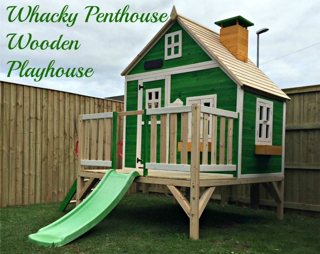 A green, whimsical Whacky Playhouse on stilts with a slanted roof, white trim, small porch, and green slide sits in a fenced garden. Text reads "Whacky Penthouse Wooden Playhouse by Big Game Hunters.
