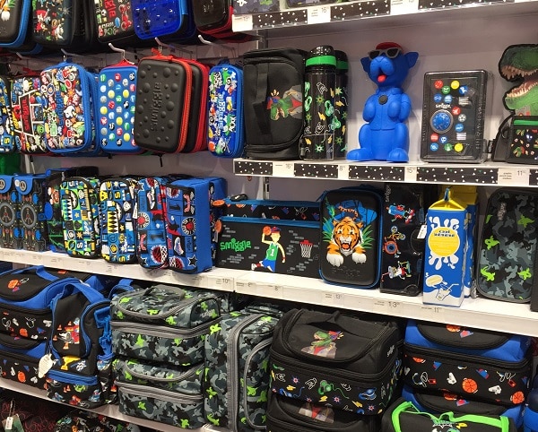 Shelves filled with colourful children’s lunchboxes, water bottles, and bags featuring fun designs like robots, animals, dinosaurs, and video game themes. Find the perfect #SmiggleXmasParty accessory from these neatly arranged, vividly patterned items.