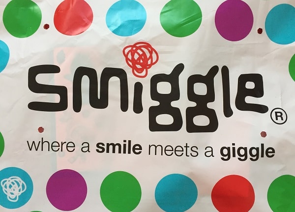 A colourful polka dot background with the Smiggle logo and tagline: "where a smile meets a giggle." The word "smile" is in black, "giggle" in bold, playful font. Perfect for the festive #SmiggleXmasParty!.