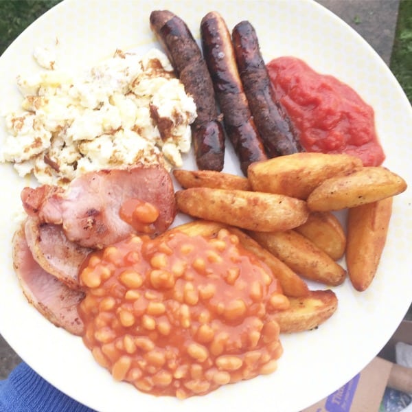 A plate with scrambled eggs, three HECK sausages, grilled tomato sauce, potato wedges, baked beans in tomato sauce, and rashers of bacon—a true Full Heck Deck breakfast.