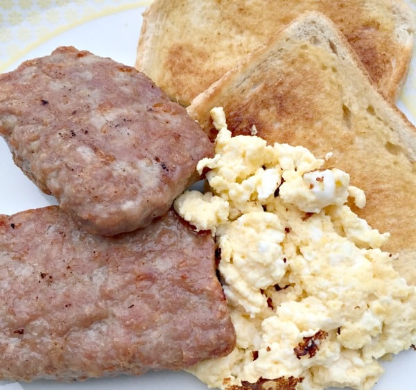 A Heck Deck breakfast plate features two pieces of HECK sausage, a serving of scrambled egg, and two toasted bread triangles.