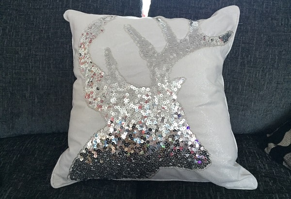 A white cushion with a shiny silver sequin stag head design adds a festive touch to your home décor, beautifully placed on a dark grey sofa—perfect décor for Christmas or stylish house décor year-round.