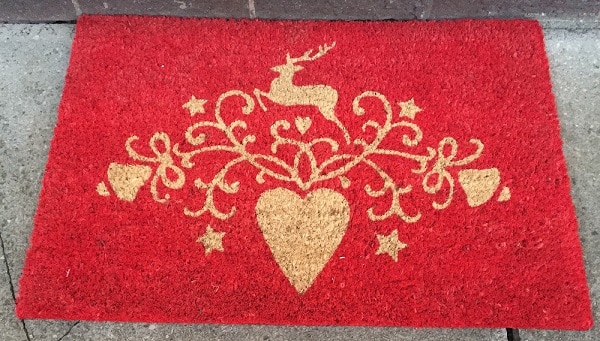 A red Christmas doormat featuring a gold design with a deer above a large heart, surrounded by swirls, stars, and smaller hearts—perfect festive decor for your home.