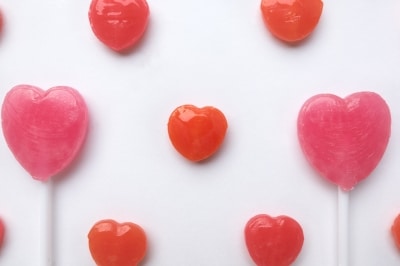 Heart-shaped pink and red lollipops are arranged in a playful pattern on a white background, making sweet gifts for women or a charming touch to your Valentine’s Day celebration.
