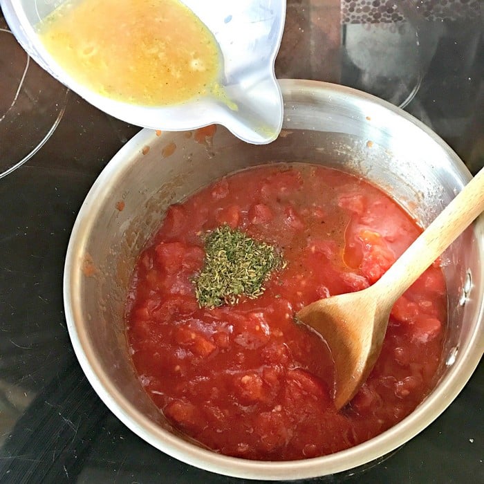 A bowl of tomato sauce with herbs and a wooden spoon sits on a hob in the WW Smart Kitchen. A measuring jug pours a yellow liquid, likely beaten eggs, into the sauce—perfect for cooking healthy meals.
