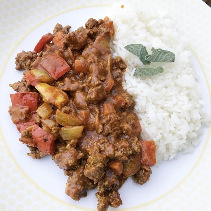 A plate with white rice garnished with fresh herbs sits next to a serving of minced beef stew with red peppers, onions, and a rich tomato-based sauce—perfect for Cooking Healthy Meals in your WW Smart Kitchen.