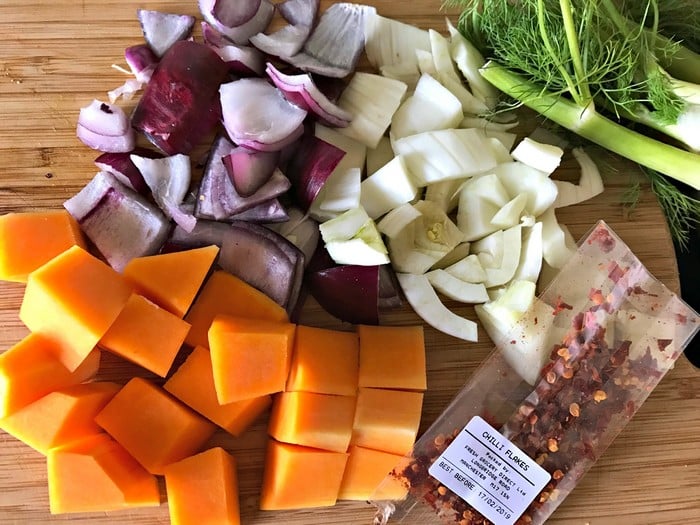 Chopped red onion, white fennel, and orange butternut squash are arranged on a wooden chopping board next to a sprig of fennel and a packet of dried chilli flakes—perfect for creating healthy meals in your WW Smart Kitchen.