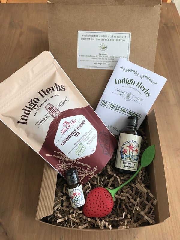 A perfect Mother’s Day gift box for your 2017 Gift List: includes camomile flower tea, two essential oils, a strawberry-shaped tea infuser, and an "Indigo Herbs" leaflet, beautifully arranged on brown shredded paper.