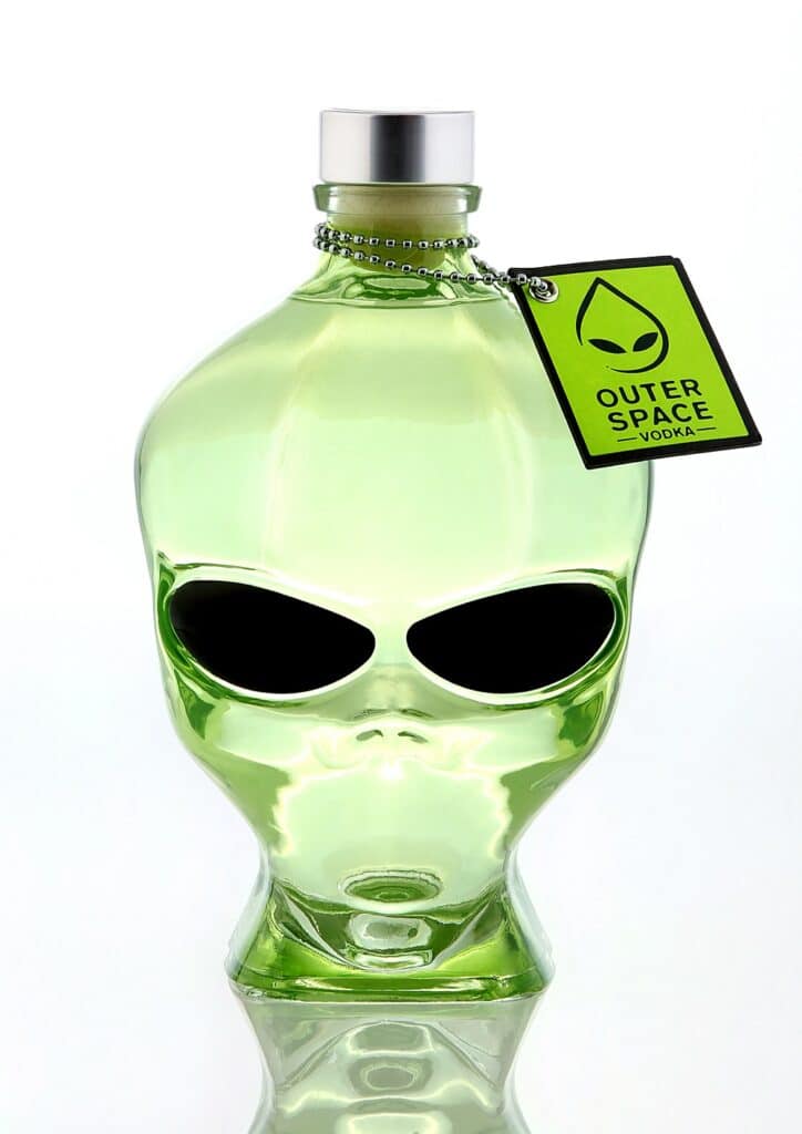 A green glass bottle shaped like an alien head with black eyes and a silver cap, labelled "Outer Space Vodka" with an alien face icon. This unique outer space vodka bottle stands out against a white background.