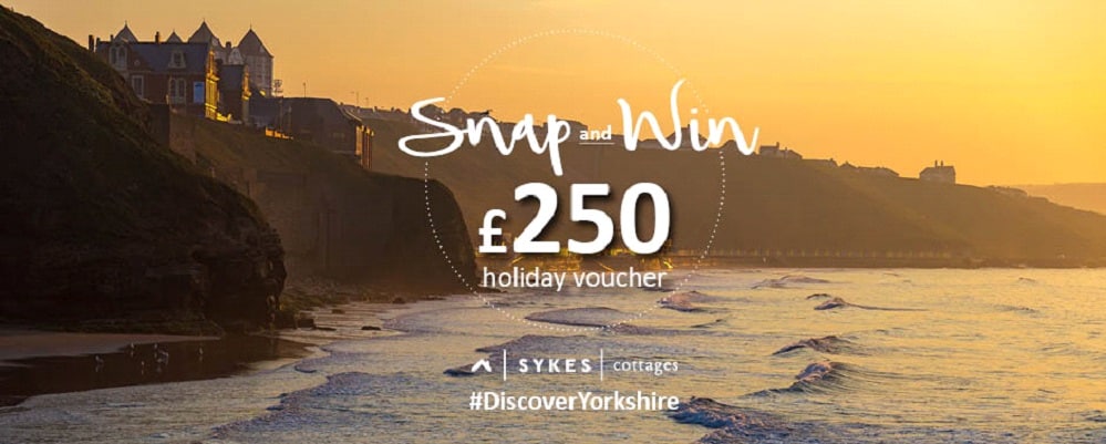 A golden sunset over the Yorkshire seaside, with waves and dramatic cliffs. Enter the "Snap and Win" competition for a chance to claim a £250 Sykes Cottages holiday voucher! Hashtag: #DiscoverYorkshire.