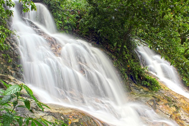Water cascades down a multi-tiered rocky waterfall surrounded by lush green foliage, creating a smooth, misty effect—reflecting the calm many women seek when trying to control emotions or manage binge eating.
