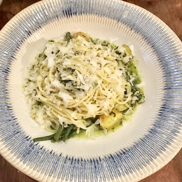 A plate of spaghetti with pesto sauce, green beans, and potatoes, topped with grated cheese, served in a cream and blue-rimmed bowl on a wooden surface—perfect for the Super Lunch Menu at Jamie’s Italian.