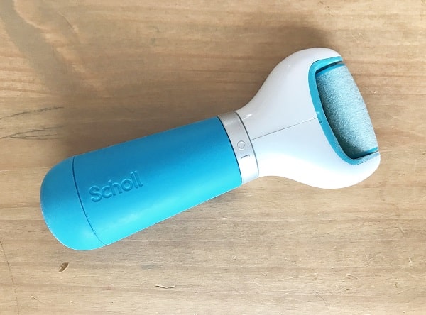 A blue and white Scholl electronic foot file with a roller head is placed on a wooden surface—perfect for achieving a salon look at home as part of your body essentials.