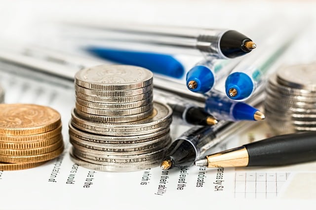 Stacks of coins and several pens lie on financial documents, evoking themes of accountancy or financial planning—ideal for illustrating how to save money when buying online.