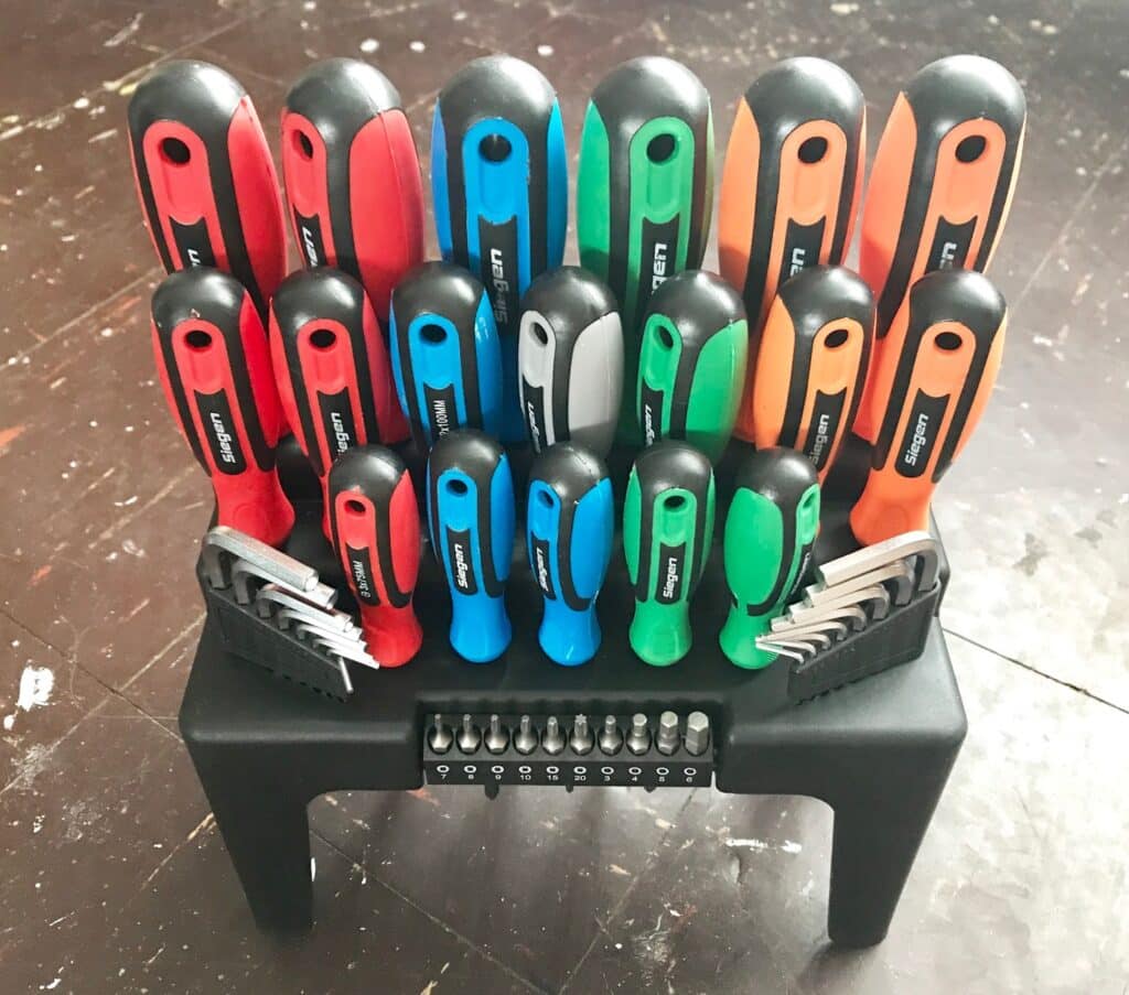 A set of assorted DIY tools with colourful handles (red, blue, green, orange, and black) organised in a black plastic stand, with screwdriver bits arranged at the bottom. The perfect choice for anyone buying tools for home projects.