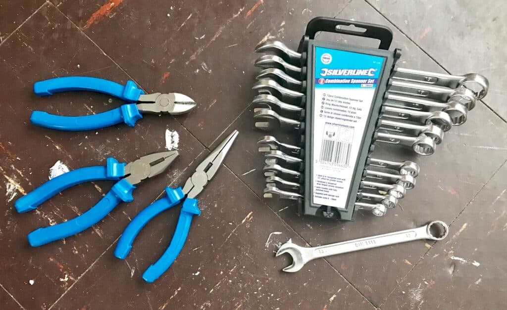 Three blue-handled pliers and a Silverline combination spanner set are laid out on a brown wooden floor. Perfect for your DIY needs, the tools are arranged neatly, with one spanner set apart from the rest.