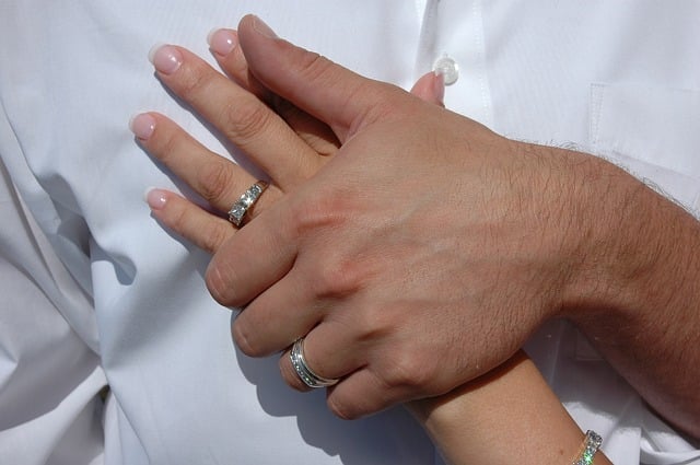 A close-up of two hands with wedding rings, gently resting on each other against a white shirt, symbolising marriage or commitment—perfect inspiration when choosing an outfit for a wedding of a different culture.