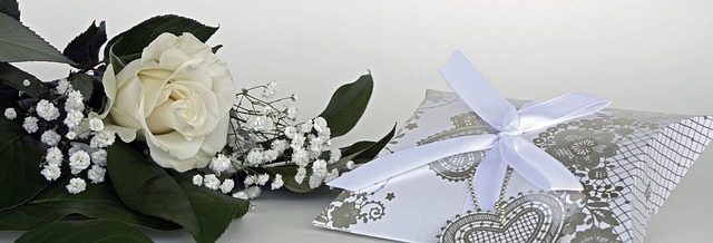 A white rose with greenery and baby's breath lies next to a decorative silver gift box—an elegant touch for bridesmaids seeking money-saving tips on beautiful yet affordable wedding details.