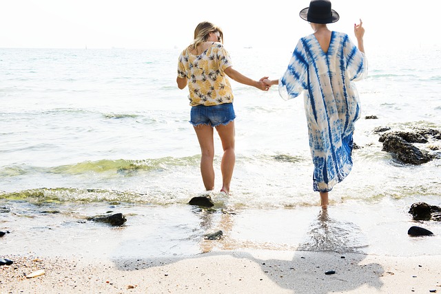 Two people walk hand in hand along a sandy beach towards the water, seeking solace and connection whilst living with depression. Waves gently reach their feet as they find comfort in each other’s presence, backs to the camera.