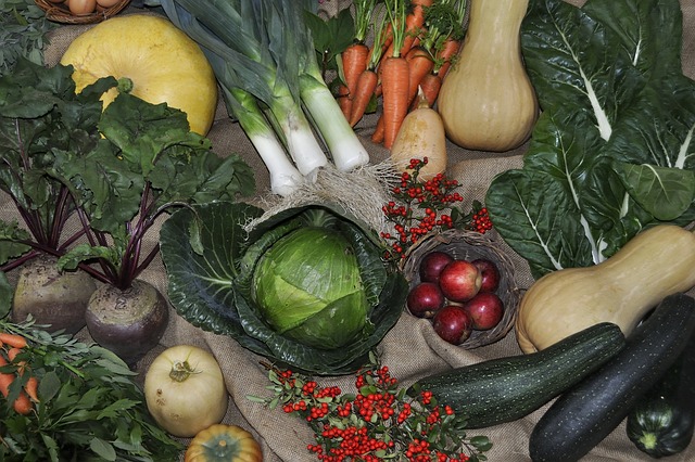 A colourful array of fresh vegetables and fruits displayed on hessian, perfect for Companion Planting enthusiasts—cabbage, carrots, leeks, squash, courgettes, beetroot, leafy greens, apples, tomatoes, and red berries await your Gardening Diaries.