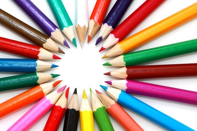 Coloured pencils arranged in a circular pattern with their sharpened tips pointing inward, forming a ring on a white background. This vibrant display highlights the benefits of colour in early years education and creative learning.